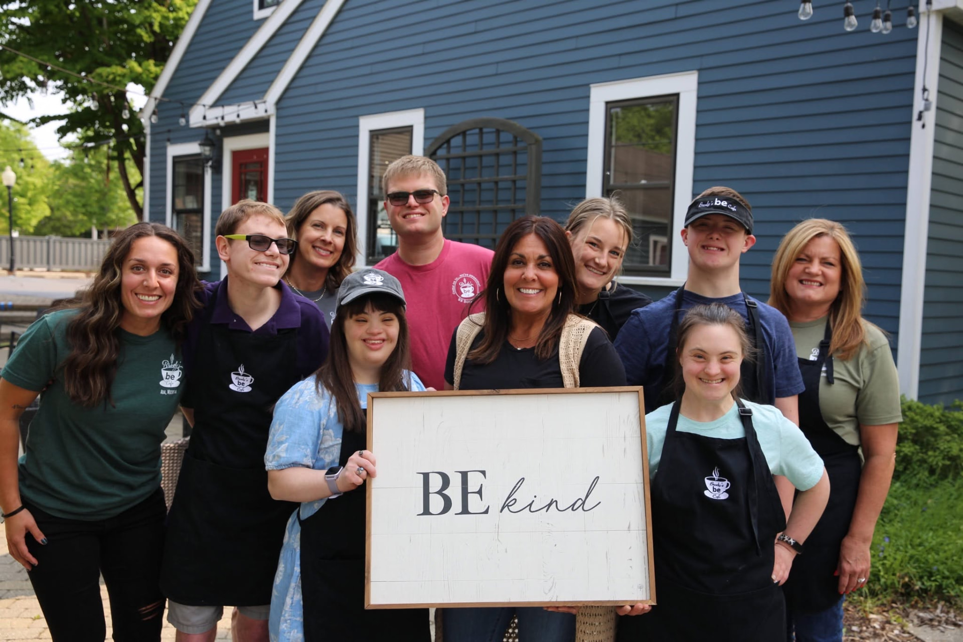Be Café Beristas and team members gathered outside a café holding a Be Kind sign